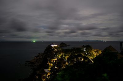 Illuminated hill by sea against cloudy sky