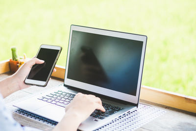 Cropped image of person using mobile phone while working on laptop