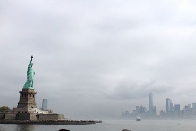 Statue of liberty by hudson river against cloudy sky