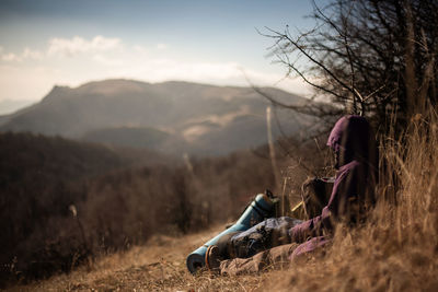 Woman sitting by plants against mountain