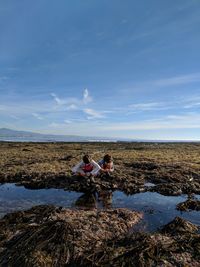 Friends crouching at beach against sky