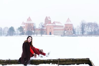 Portrait of smiling woman sitting on snow covered retaining wall
