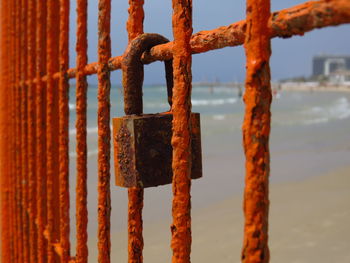 Close-up of lock on rusty metallic gate against beach