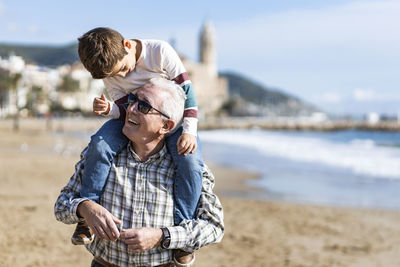 Happy senior man giving piggyback ride to grandson at beach