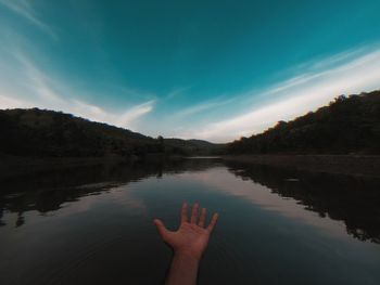 Reflection of hand in lake against sky