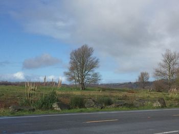 Road passing through field against cloudy sky