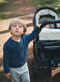 Boy holding stroller with baby boy at park