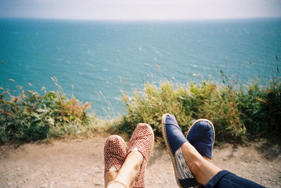 Low section of man and woman relaxing on land by sea
