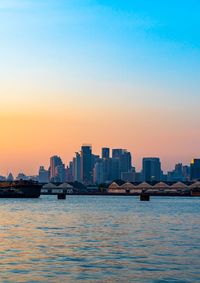 Sea by buildings against sky during sunset