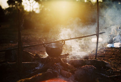 Cooking utensil hanging over firewood in forest during sunset