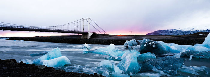 Suspension bridge over sea against cloudy sky during winter at sunset