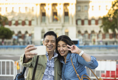 Smiling man with woman taking selfie through mobile phone on footpath