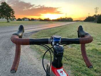 Bicycle on road amidst field against sky during sunset