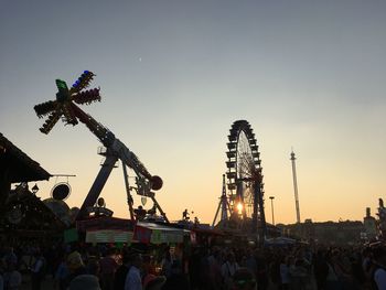 People at amusement park against sky during sunset