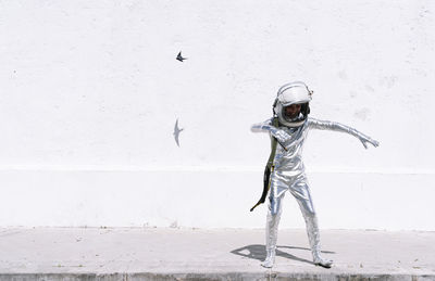 Boy in astronaut costume playing while standing against wall in city