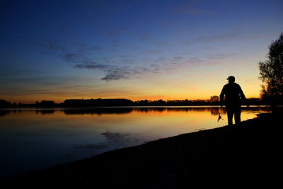 Rear view of silhouette man by lake against sky during sunset