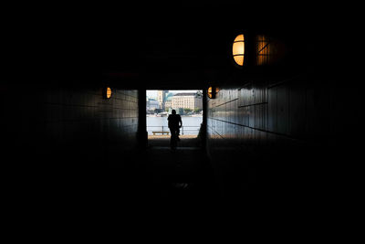 Rear view of silhouette man walking in illuminated tunnel