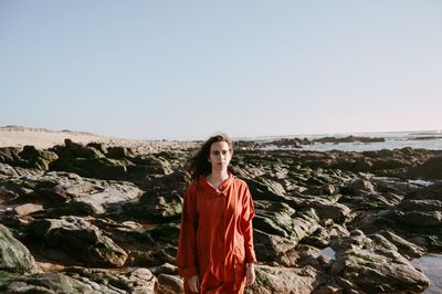 Portrait of young woman standing on rock against clear sky