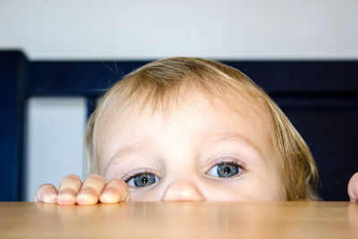 Portrait of toddler hiding behind table at home