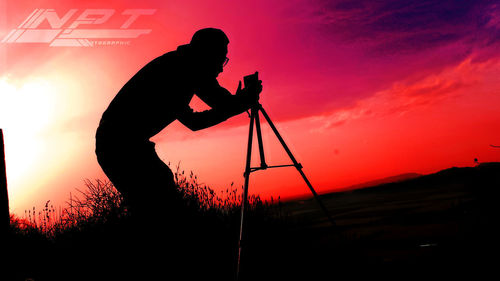 Silhouette man photographing orange camera against sky during sunset