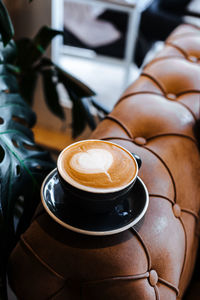 Black cup of cappuccino with latte art on wooden background. green monstera plant at cafe