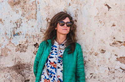 Portrait of woman wearing sunglasses standing against wall