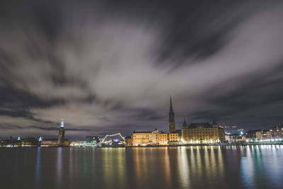 Illuminated cityscape against cloudy sky at night