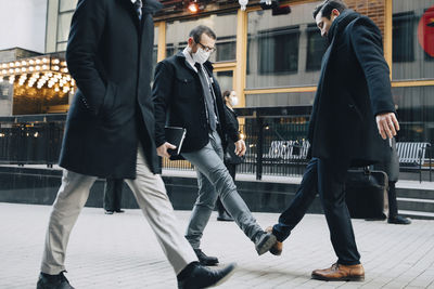 Businessmen greeting with foot tap on footpath in city during pandemic