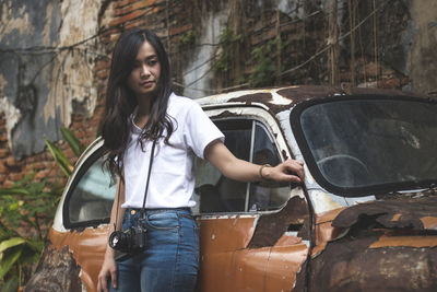 Young woman smiling while standing by abandoned car