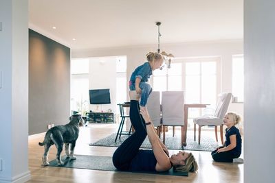 Smiling mother lifting happy daughter while lying on exercise mat at home