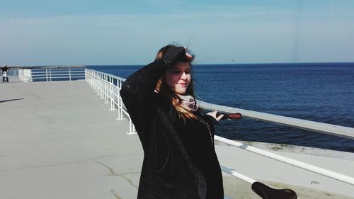 Woman shielding eyes on pier over sea against sky