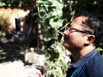 Profile view of man wearing eyeglasses while standing against plants