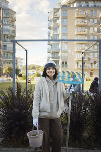 Portrait of smiling teenage girl holding rake and bucket