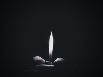 Close-up of hand holding lit candle against black background