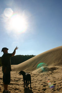 Boy with dog standing on sand against clear sky