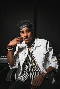 Portrait of young man standing against black background