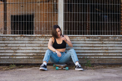 Woman with skateboard sitting by fence