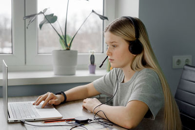 Teenage student girl in headphones having online lesson at home