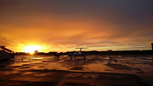 Airplane at wet runway against cloudy sky during sunset