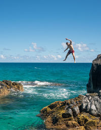 Low angle view of shirtless man jumping in sea from cliff against sky