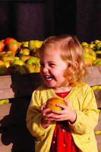 Cheerful girl looking away while holding apple against cart