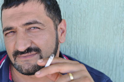 Portrait of man smoking cigarette against wall