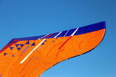 Low angle view of part of an orange mostov statue against blue sky