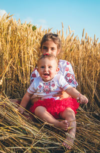 Portrait of cute sibling sitting at farm