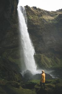 Man standing by waterfall against sky