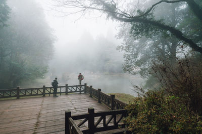 People on footbridge against sky during winter
