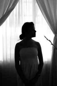 Woman in dress standing by window curtains in darkroom