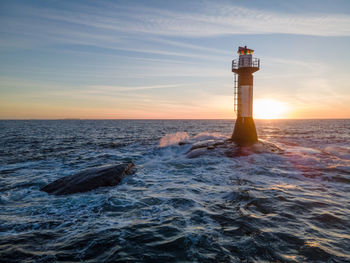 Lighthouse by sea against sky during sunset