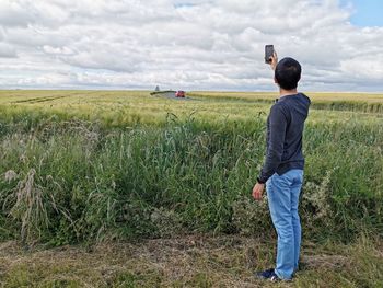 Full length rear view of man photographing on land against sky