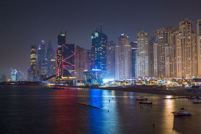 Night city dubai in uae. illuminated modern buildings by sea against sky at night